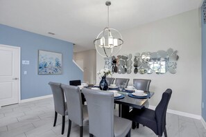 A dining area with a chandelier, a wall-mounted mirror art piece, and a vase with flowers.