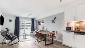 A modern apartment with a dining area, kitchen, and a living space with a sofa and a TV.