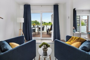 Relax in this stylish living room with a sofa, round table, and potted plant, opening to a balcony with a dining set and city views.