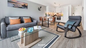 A modern living room with a glass coffee table, grey sofa, and a dining area with a wooden table and chairs. - Meerzeit - Shower room, covered balcony, garden furniture, TV, washing machine (Damp)