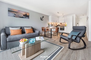 A modern living room with a glass coffee table, grey sofa, and a dining area with a wooden table and chairs.