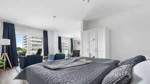 A modern bedroom with a large bed, a wardrobe, a desk, and a view of a building with scaffolding.