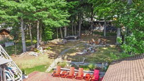 A backyard with a stone fire pit, wooden deck, and outdoor seating area. - Waterfront 5 BR Home with Dock Slip (queensbury)