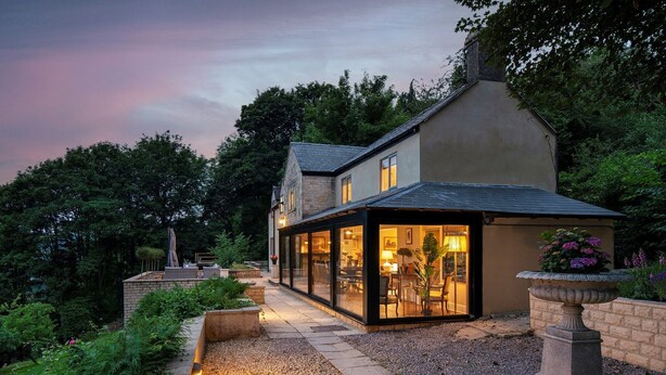A modern house with a glass conservatory, surrounded by a garden and a stone pathway. - Beautiful hill side house with stunning valley view in the centre of Cotswolds (Chalford)