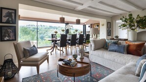 A spacious living room with a large window, a dining area, and a cozy seating area with a coffee table. - Beautiful hill side house with stunning valley view in the centre of Cotswolds (Chalford)
