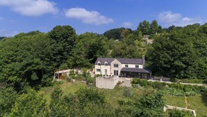 A two-story house with a stone facade, a large front porch, and a view of the surrounding forest. - Beautiful hill side house with stunning valley view in the centre of Cotswolds (Chalford)