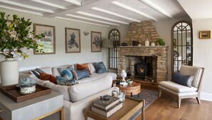 A cozy living room with a stone fireplace, a sofa with patterned cushions, and a wooden coffee table. - Beautiful hill side house with stunning valley view in the centre of Cotswolds (Chalford)