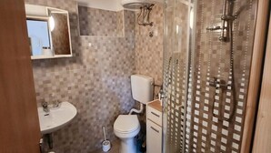 Ett badrum med en dusch som är avskärmad med glasväggar, en toalett, ett handfat och en spegel.