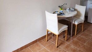En matplats med två vita stolar, ett runt bord, en platt-TV som är monterad på väggen och en inramad tavla ovanför bordet.