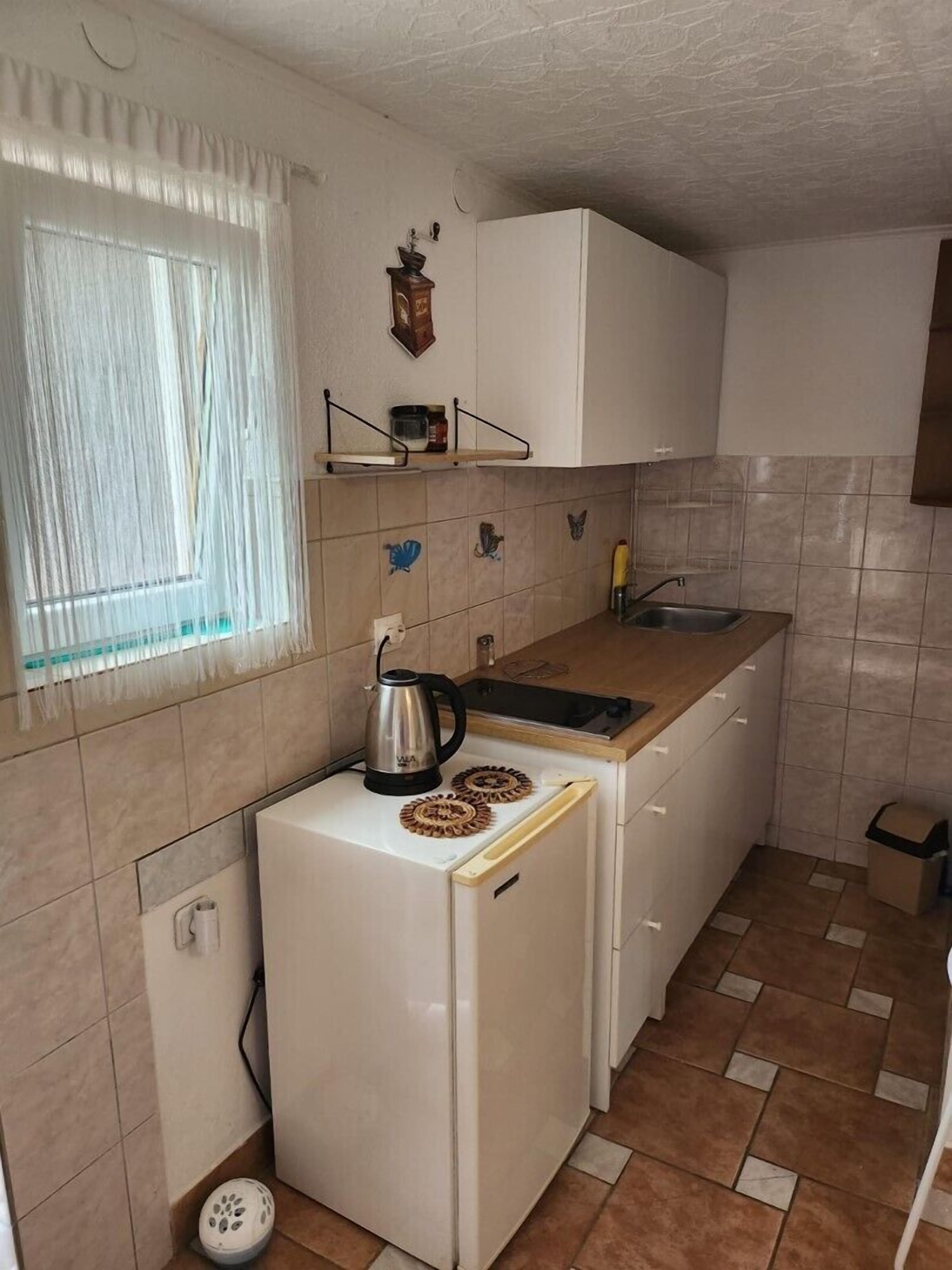 Eine kleine Küche mit Kühlschrank, Herd, Spüle und einem Fenster mit Vorhängen.