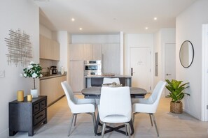 A modern kitchen with white cabinets, a dining table with four chairs, and a small side table with candles. - 2BR Penthouse Ocean View at Hyde Beach House by RedAwning (Hollywood)