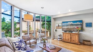 A spacious living room with a large window, a flat-screen TV, and a wooden cabinet. - Napili Gardens B7 3 Bedroom 3 Townhouse by RedAwning (Lahaina)