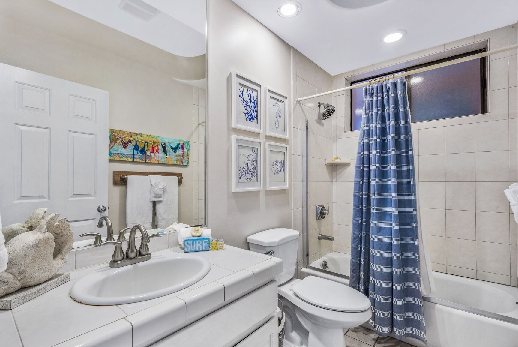 Un baño moderno con lavamanos doble, inodoro y bañera. Hay cuadros enmarcados en la pared, un perchero para toallas y una cortina de ducha.