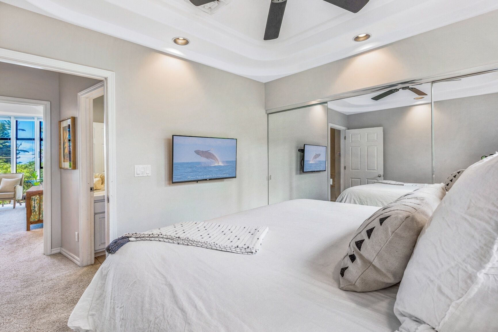 A bedroom with a large bed, a television mounted on the wall, and a door leading to a balcony.