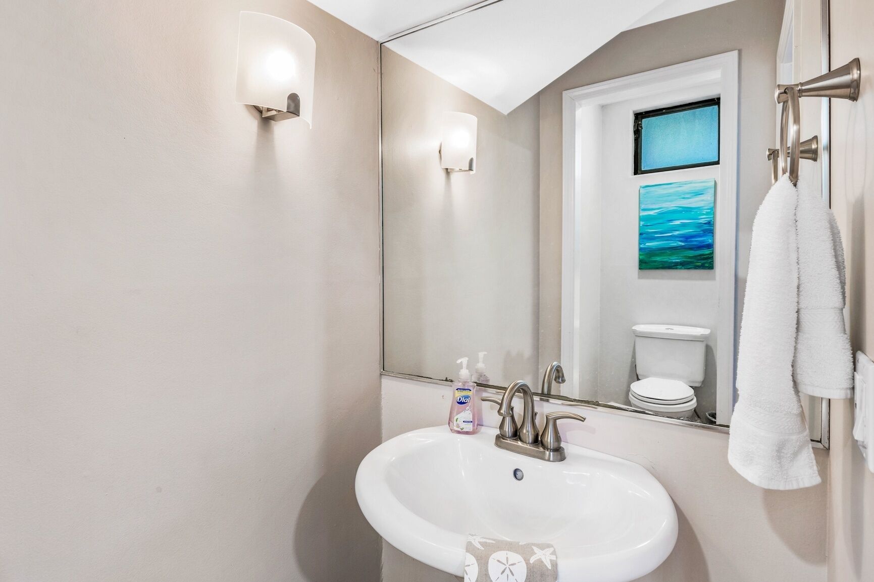 A bathroom with a white sink, a mirror, a toilet, and a towel rack.