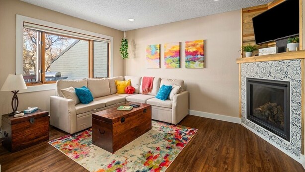 A living room with a sectional sofa, a wooden coffee table, a fireplace, and a TV mounted above it. - Whistler Village - Redwood 10 2 Bedroom Condo by RedAwning (Steamboat Springs)