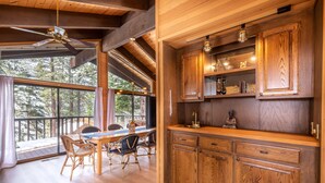 A wooden kitchen with built-in cabinets, a dining area with wicker chairs, and a large window overlooking trees. - Beautiful 3-Bedroom Contemporary Mountain Home in Northstar by RedAwning Save 10% on 3 Nights, 15% on 5 Nights! (Truckee)