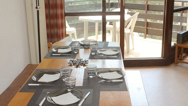 Een eettafel gedekt met borden, glazen en bestek, geplaatst bij een raam met uitzicht op tuinmeubilair.