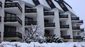 Een meerlaags gebouw met balkons, omgeven door met sneeuw bedekte struiken.