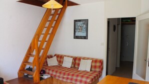Een gezellige kamer met een houten trap, een geruit bankstel en een klein tafeltje.