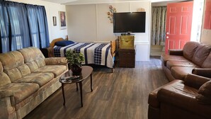 Una sala de estar con sofá, mesa de centro, televisor, cama y puerta.