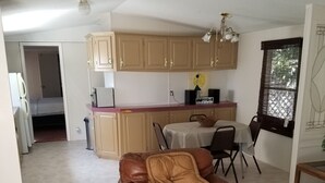 Una sala de estar con un sofá de cuero marrón, un comedor con mesa y sillas, y una cocina con armarios color beige y un microondas.