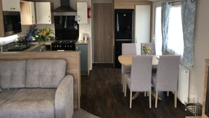 Una cocina moderna con estufa a gas, horno empotrado y campana extractora negra. Cuenta con un comedor con mesa de madera y sillas tapizadas en gris. Un sofá gris se encuentra en primer plano.