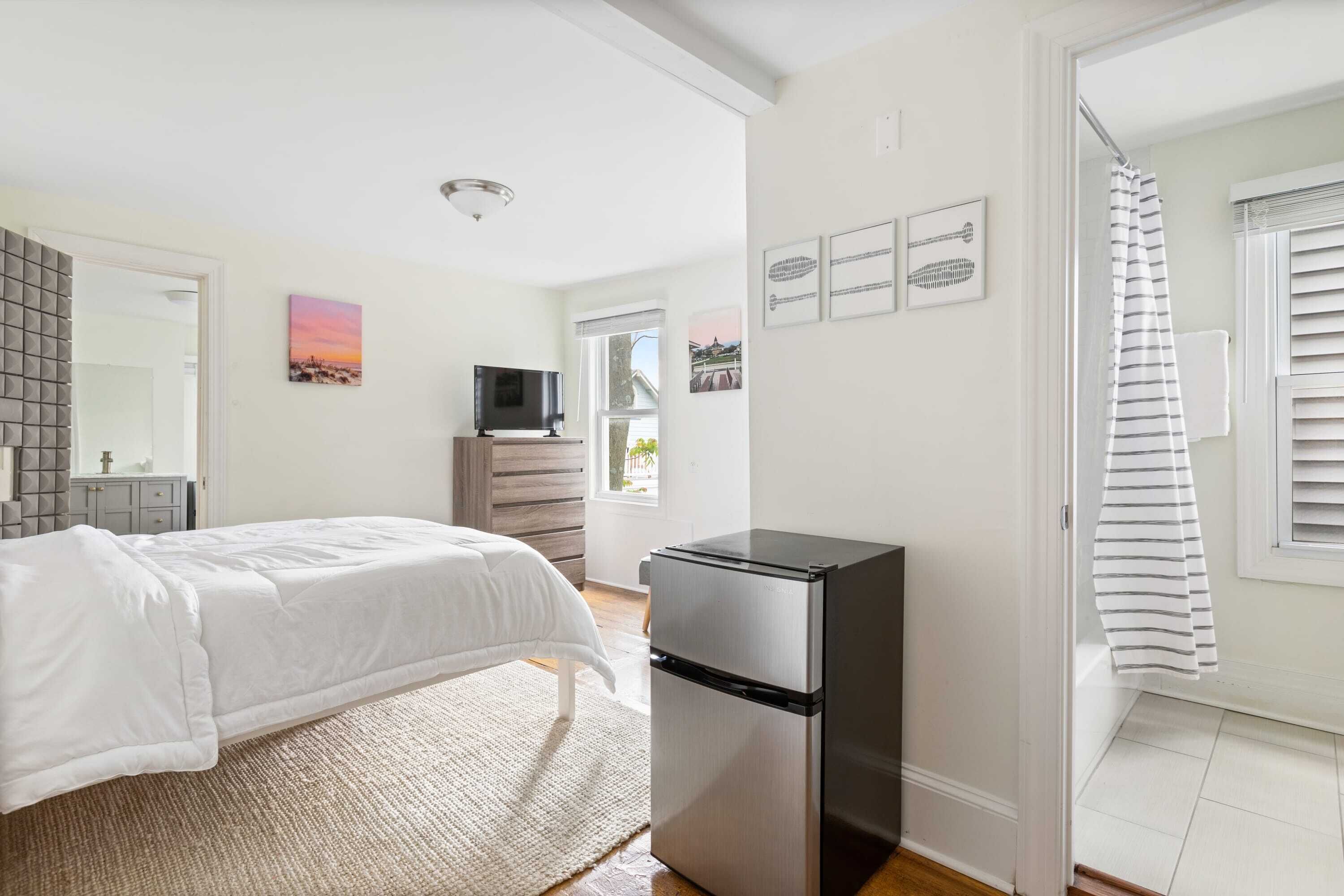 Un dormitorio con cama, un refrigerador pequeño, televisor y una ventana con persianas.
