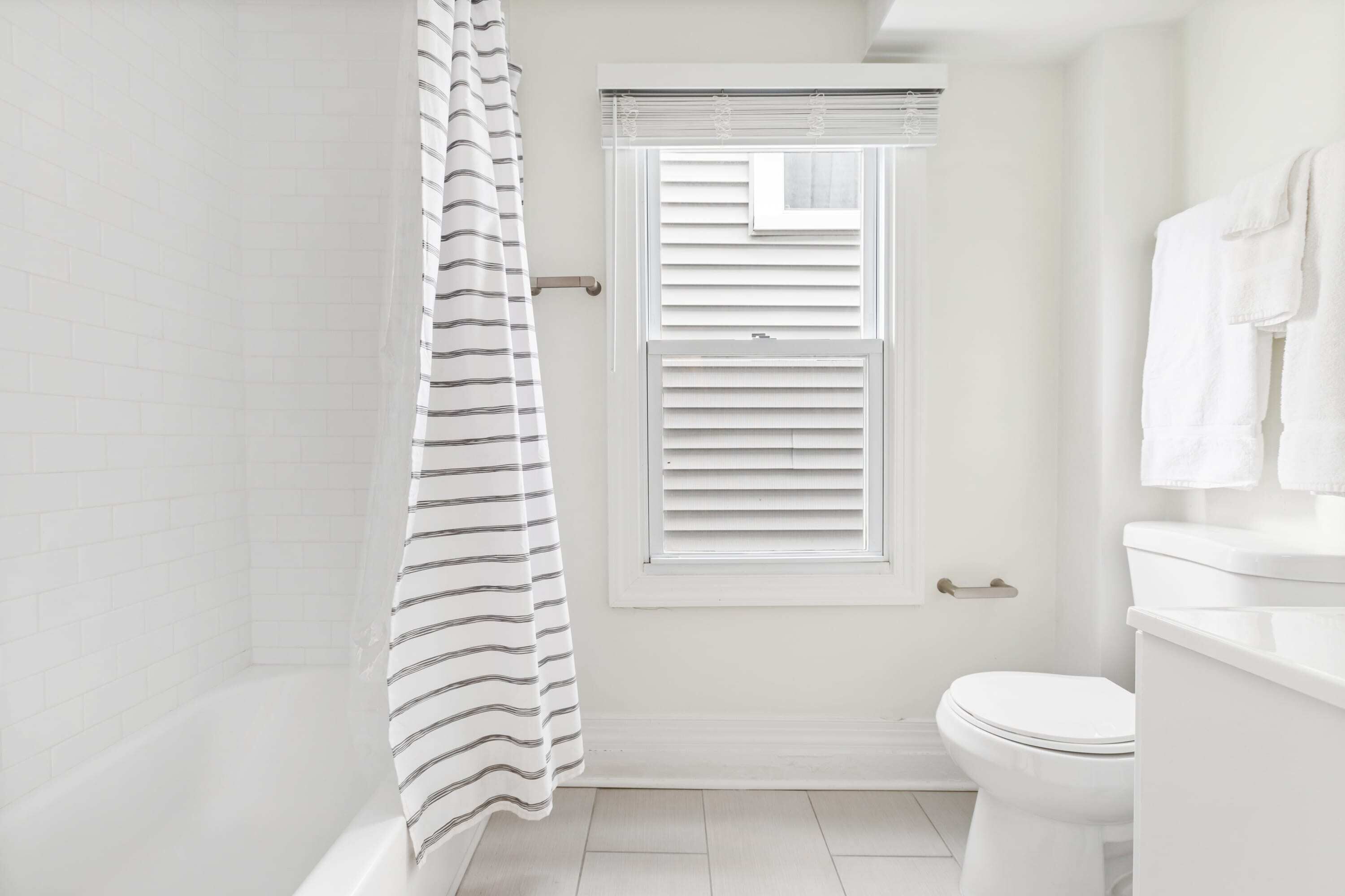 Une salle de bain avec une douche, des toilettes et une fenêtre avec des stores.