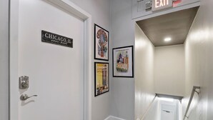 Un pasillo con una puerta que indica "CHICAGO, IL", un cartel enmarcado con motivos de Chicago y una señal de salida.