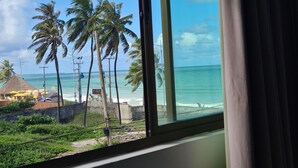 A view from a window overlooking a beach with palm trees and a clear sky. - Ritz Suítes Maceió Flat particular (Maceió)