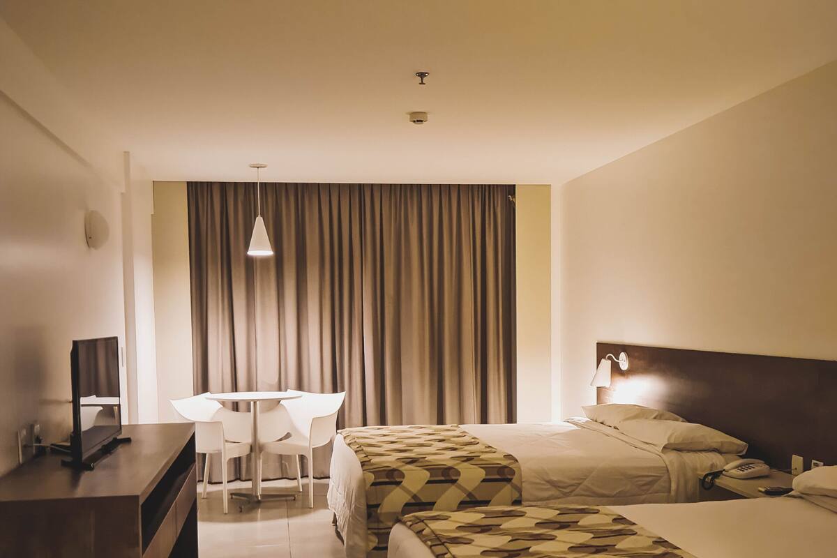 A hotel room with two beds, a desk with a chair, a television, and a window with curtains.