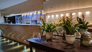 A reception area with a counter, potted plants, and a statue. - Ritz Suítes Maceió Flat particular (Maceió)