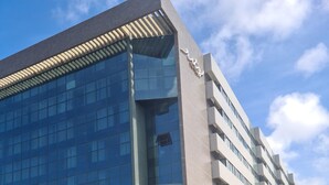 A modern hotel with a glass facade, a sign for 'Suites', and a well-maintained garden area. - Ritz Suítes Maceió Flat particular (Maceió)