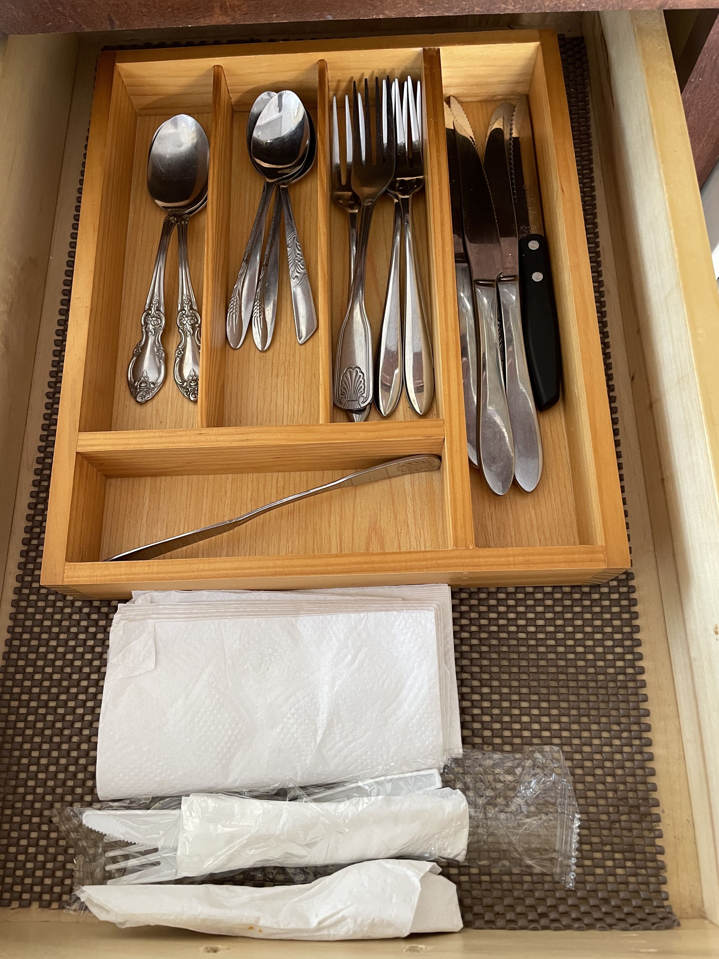 Un cajón con cubiertos ordenados, incluyendo cucharas, tenedores y cuchillos, y un cuchillo de plástico.