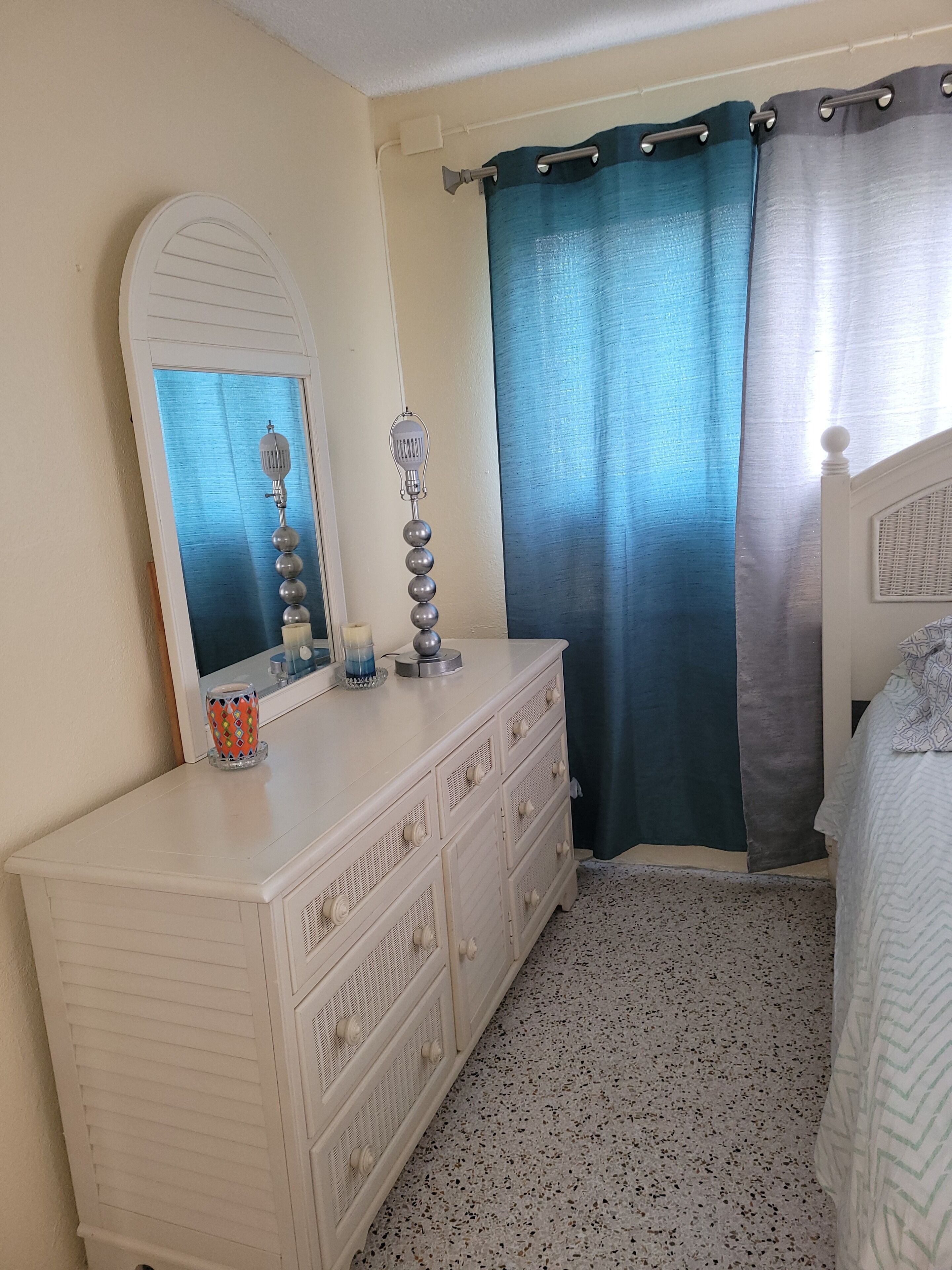 A bedroom with a dresser, a mirror, a lamp, and a bed.