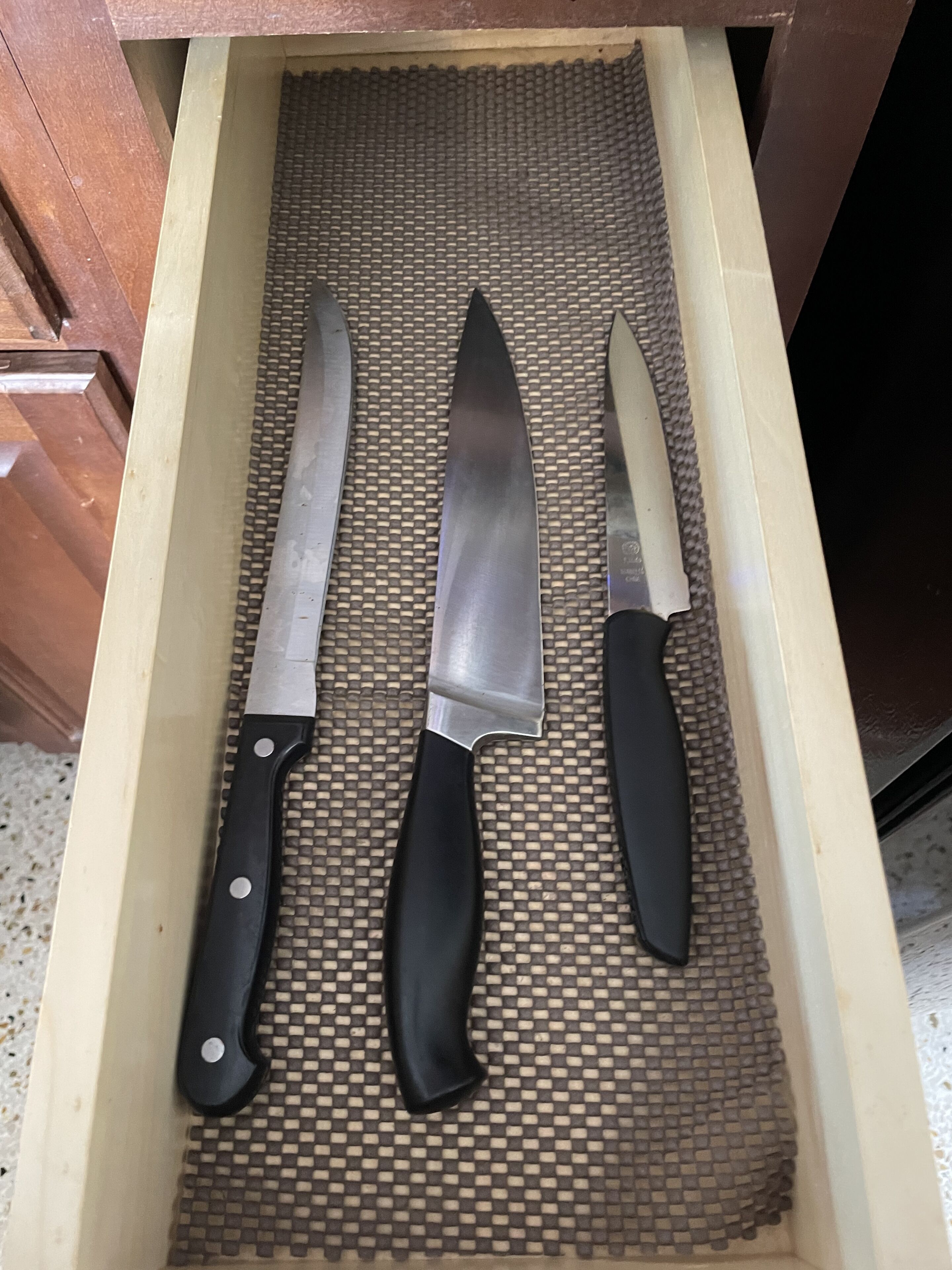 A drawer containing three kitchen knives with black handles.