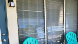 A porch with two turquoise Adirondack chairs, a small round table with a vase, and a door with a metal handle. - The Island Life Condo@ Long Reef with Separate Bedroom + True Ocean View (Christiansted)