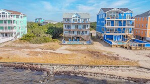 A beachfront hotel with multiple floors, outdoor seating, and a pool area. - Soundfront w/ Pool, Hot Tub, Elevator, Game and Media Rooms, Windsports Access (Avon)