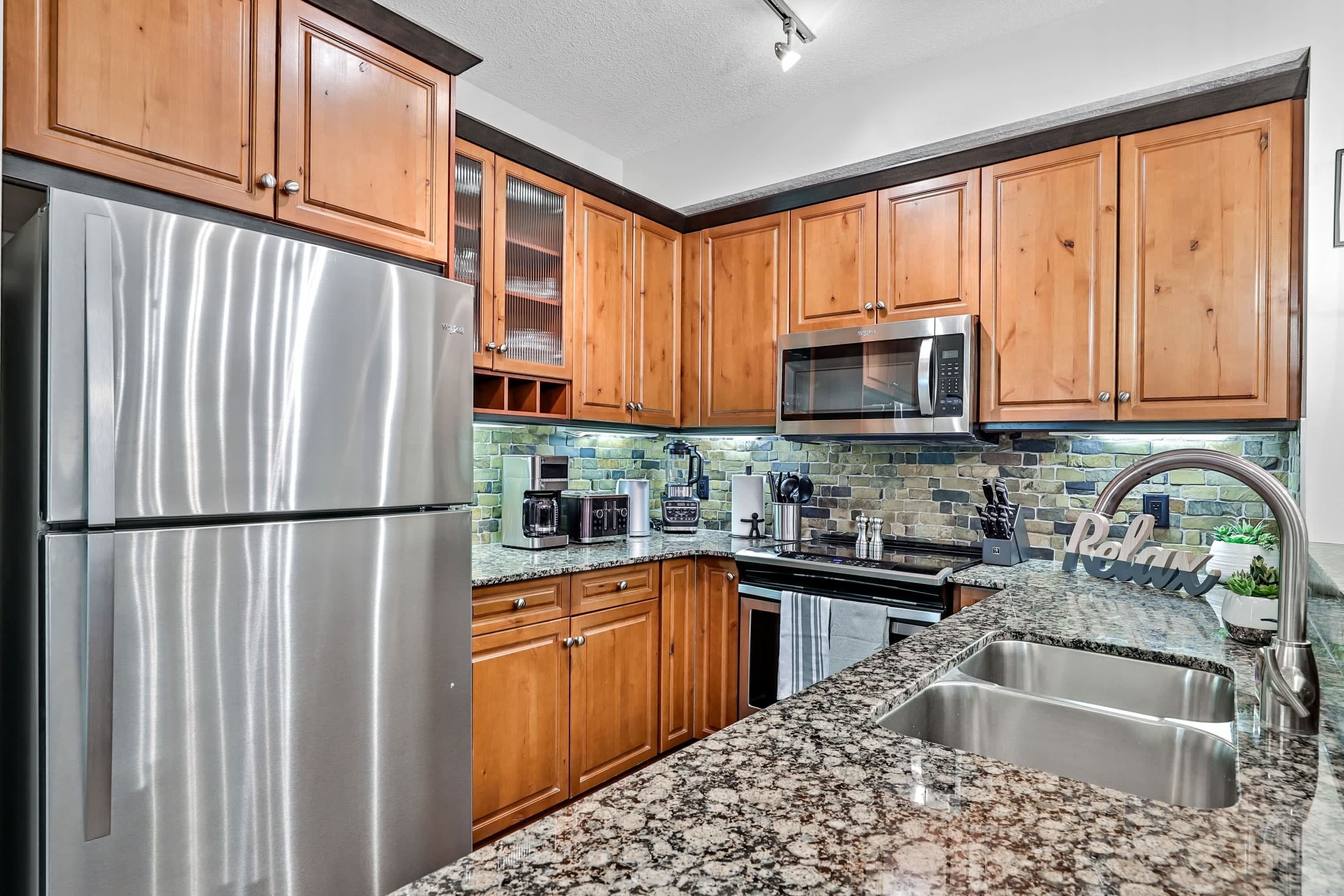 A kitchen with wooden cabinets, stainless steel appliances, a granite countertop, and a backsplash with a mosaic tile design.