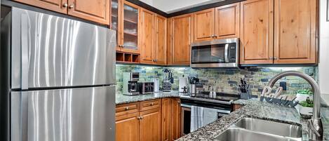 A kitchen with wooden cabinets, stainless steel appliances, a granite countertop, and a backsplash with a mosaic tile design.