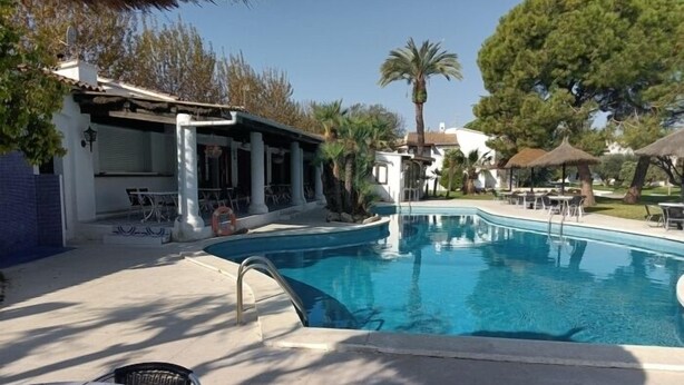 A swimming pool with lounge chairs and umbrellas, surrounded by buildings and trees. - R121 Apartamento Alorda Park (Calafell)