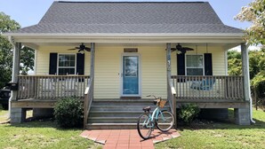 Ein zweistöckiges Haus mit einer Veranda, einem Fahrrad und einem Schild mit der Aufschrift 'NO NAME COTTAGE'.