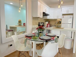 A modern kitchen with white cabinets, a glass dining table, and white chairs.