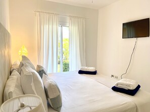 Habitación de hotel con cama, almohadas, televisor de pantalla plana montado en la pared y ventana con cortinas.