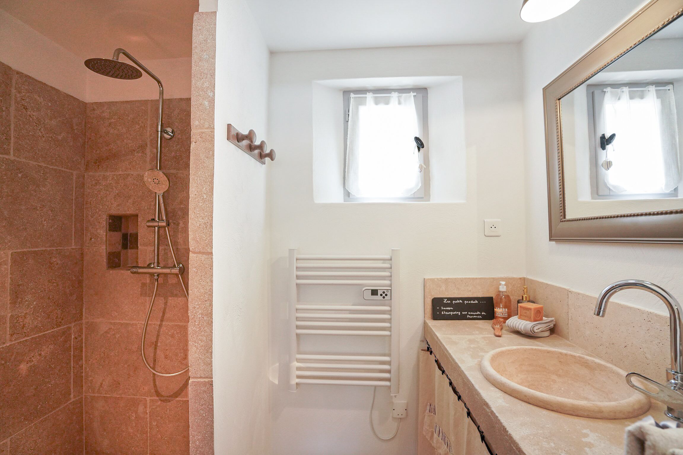 Une salle de bain avec une douche, un lavabo, un porte-serviettes et une fenêtre.