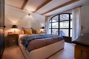 A bedroom with a large bed, two bedside lamps, a nightstand, and a window with a view. - Cottage-Ensuite with Bath-Garden view-Cottage Mirabeau (Aix-en-Provence)