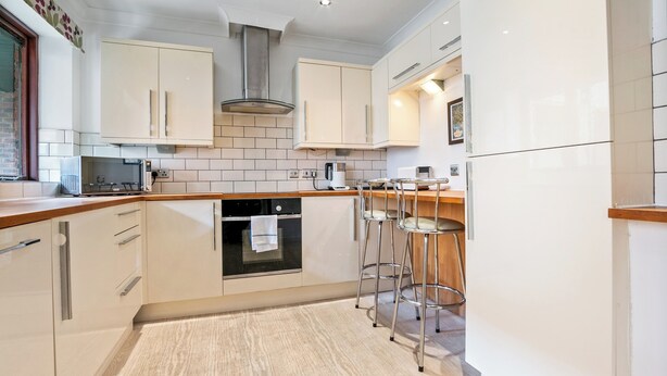 A modern kitchen with white cabinets, a stainless steel range hood, a built-in oven, and a bar area with stools. - 5 St Georges House · Lovely 1-Bed Apartment Right in the Heart of York - Pass the Keys (York)
