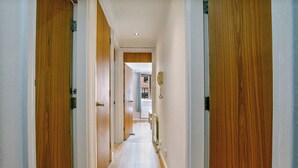 A narrow hallway with wooden doors on either side, leading to a room with a radiator and a window. - 5 St Georges House · Lovely 1-Bed Apartment Right in the Heart of York - Pass the Keys (York)