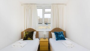 Una habitació doble amb dos llits, una finestra amb cortines, una làmpada i una petita taula de nit de fusta.
